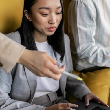 Asian woman in blazer focused on using laptop, representing technology and teamwork.