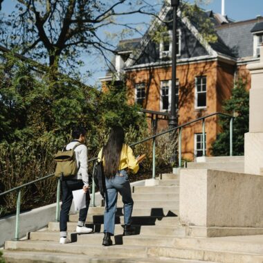 Two students walking up stairs on a sunny day at a university campus.