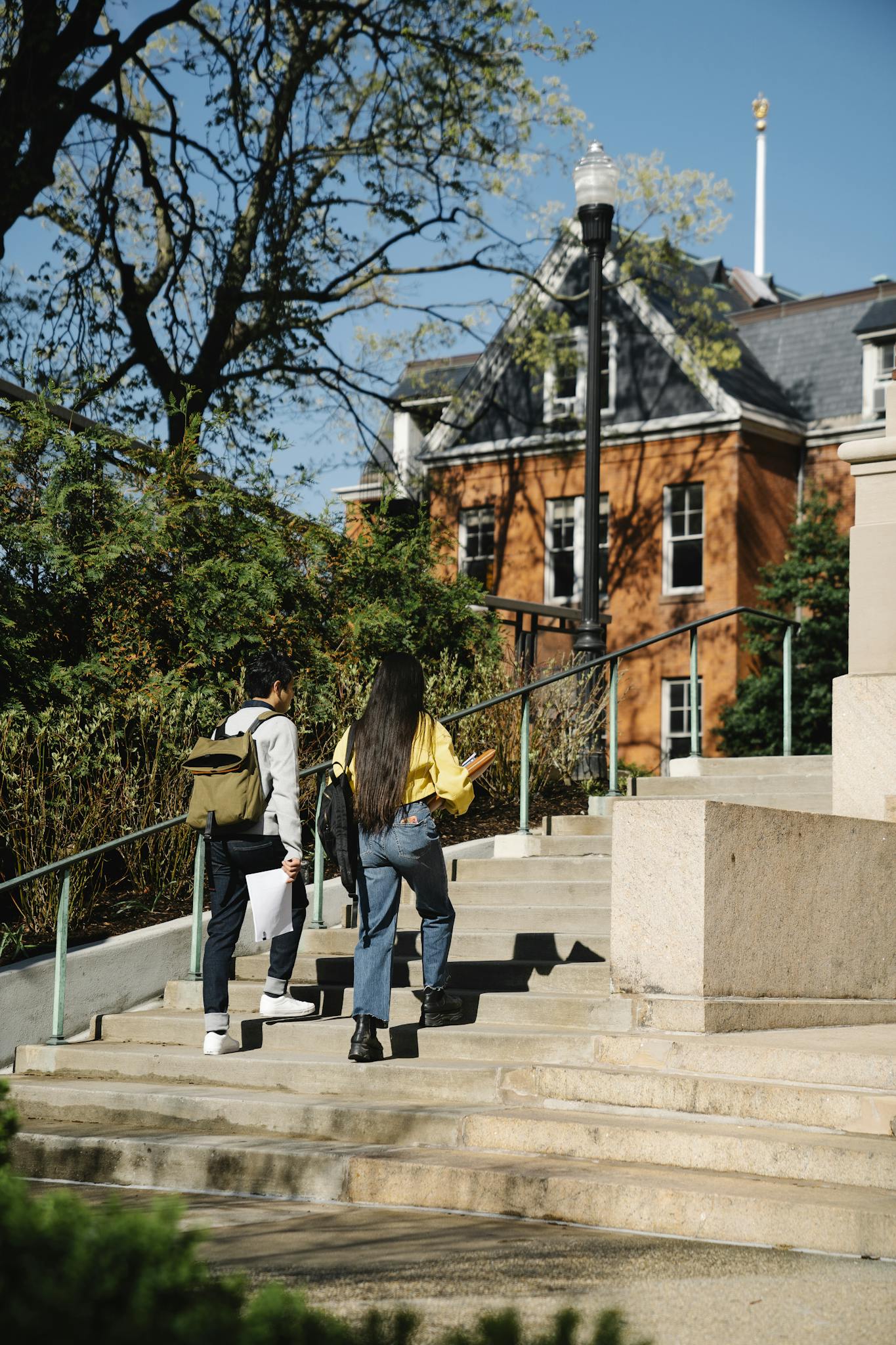 Two students walking up stairs on a sunny day at a university campus.